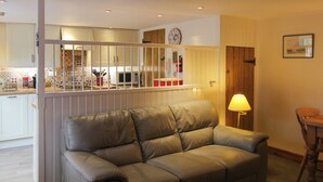A living room with a beige sofa, a dining table with chairs, a lamp, and a kitchen area visible through a glass partition. - 2 bedroom accommodation in Docking (Docking)