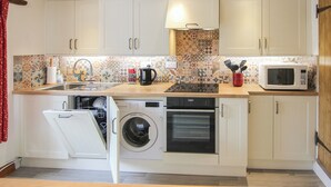 A compact kitchen with white cabinets, a built-in washing machine, an oven, a microwave, and a sink. - 2 bedroom accommodation in Docking (Docking)