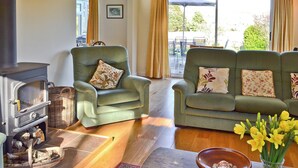 A cozy living room with a fireplace, two green armchairs, a sofa, a wooden coffee table, and a vase of yellow flowers. - 3 bedroom accommodation in Brighstone (Brighstone)