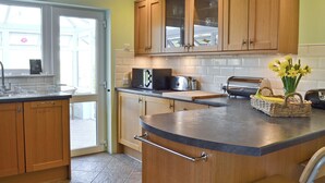 A kitchen with wooden cabinets, a microwave, a toaster, and a vase with flowers on the counter. - 3 bedroom accommodation in Brighstone (Brighstone)