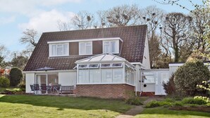 A two-story house with a conservatory, a patio with outdoor furniture, and a well-maintained garden. - 3 bedroom accommodation in Brighstone (Brighstone)