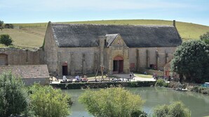 A historic stone building with a thatched roof, a small pond in the foreground, and a grassy hill in the background. - 2 bedroom accommodation in Walditch, near Bridport (Walditch, near Bridport)