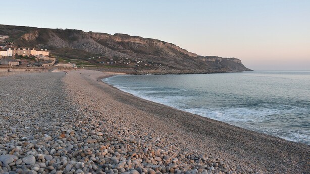 Une plage de galets bordée de maisons construites sur une falaise, d’où l’on a une vue imprenable sur la mer.