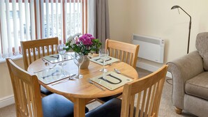 A dining table set for four with wooden chairs, a vase of flowers, and a radiator in the background.