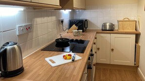 A kitchen with white cabinets, a black stove, a kettle, a toaster, and a bread box.