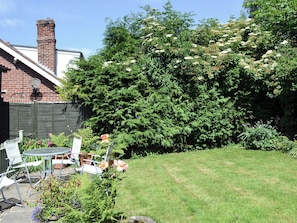 A backyard with a brick chimney, a wooden fence, and a variety of plants and flowers.