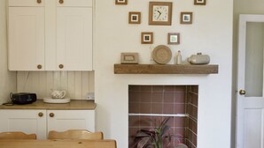 Eine Küche mit weißen Schränken, einem Holztisch, einer Uhr und einem Kamin mit Blumentopf.