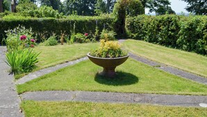 Ein gepflegter Garten mit einem zentralen Pflanzgefäß, ordentlich geschnittenem Rasen und einer Hecke im Hintergrund.
