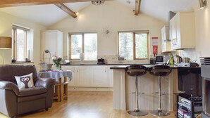 A spacious kitchen with white cabinets, a wooden ceiling, and a dining area with a leather sofa and two bar stools. - 3 bedroom accommodation in Kidderminster (Kidderminster)