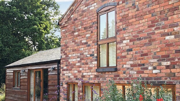 A brick house with a wooden door and windows, surrounded by a garden with various plants and flowers. - 3 bedroom accommodation in Kidderminster (Kidderminster)