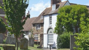 A cemetery with headstones and a pathway leading to a white building with a stone facade. - An unusual two-storey apartment with beams and an open fire. (Rye)