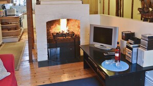 A cozy living room with a fireplace, a television, and a collection of books and DVDs on a table. - An unusual two-storey apartment with beams and an open fire. (Rye)