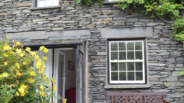 A stone building with a wooden bench outside, a door leading inside, and a window with a grid pattern. - 2 bedroom accommodation in Ambleside (Ambleside)