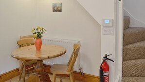 A dining area with a table, chairs, a vase with flowers, a hanging light fixture, a small painting, a thermostat, a fire extinguisher, and a staircase. - 2 bedroom accommodation in Ambleside (Ambleside)