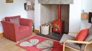 A living room with a red sofa, a grey armchair, a fireplace, a bookshelf, and a framed picture on the wall. - 2 bedroom accommodation in Ambleside (Ambleside)