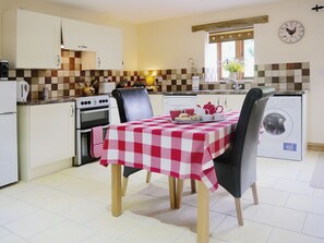 A compact kitchen with a dining table, chairs, a washing machine, and a clock on the wall. - 1 bedroom accommodation in Hartland, near Bideford (Hartland, near Bideford)