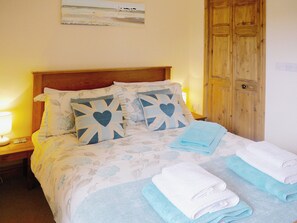 A neatly made bed with floral bedding, two pillows with heart designs, and folded towels on the bed. - 1 bedroom accommodation in Hartland, near Bideford (Hartland, near Bideford)