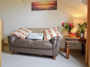 A brown leather sofa with patterned pillows, a wall-mounted painting, a small table with a vase of flowers, and a lamp. - 1 bedroom accommodation in Hartland, near Bideford (Hartland, near Bideford)