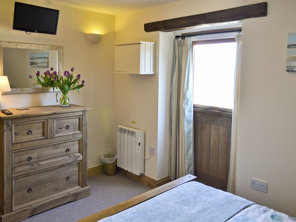 A room with a bed, a dresser, a radiator, a TV mounted on the wall, and a window with curtains.