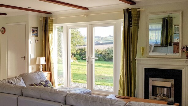 A living room with a sofa, a fireplace, and a view of the outdoors through large glass doors. - 1 bedroom accommodation in East Taphouse, near Liskeard (East Taphouse, near Liskeard)