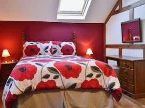 A bedroom with a bed, two bedside lamps, a wooden dresser, a mirror, and a skylight.