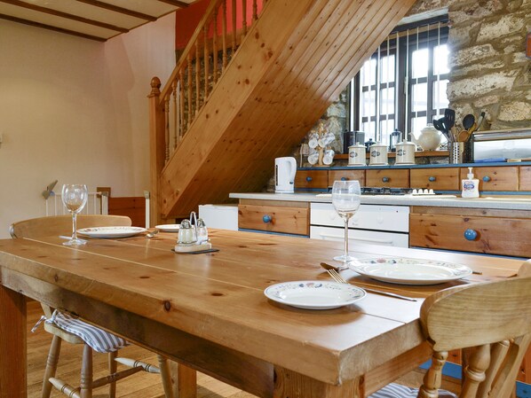 A wooden dining table with plates and glasses, a staircase, and kitchen cabinets in the background.