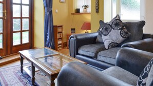 Un salon avec un canapé, une table basse en verre, une bibliothèque et une fenêtre avec des rideaux.