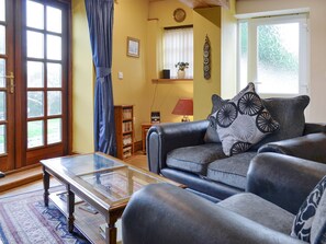 A living room with a sofa, a glass coffee table, a bookshelf, and a window with curtains.