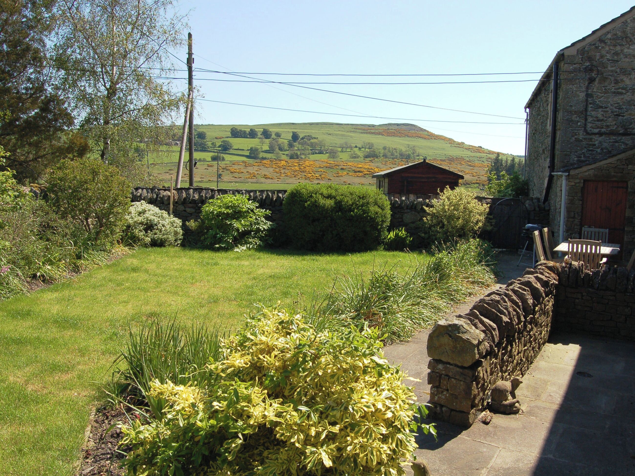 A stone wall, a wooden cabin, and a grassy field with a stone pathway.