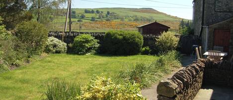 A stone wall, a wooden cabin, and a grassy field with a stone pathway.