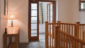 A wooden staircase with a handrail, a wooden door with glass panels, and a small table with a lamp. - 4 bedroom accommodation in Keswick (Keswick)