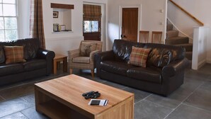 A living room with two leather sofas, a wooden coffee table, and a plaid armchair. There is a staircase leading to another level. - 4 bedroom accommodation in Keswick (Keswick)