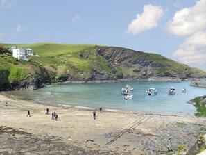 A coastal scene with boats docked at a pier, a sandy beach, and a building on a hill. - 1 bedroom accommodation in St Kew, near Port Isaac (St Kew, near Port Isaac)