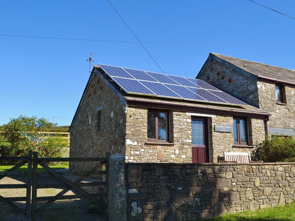 A stone building with a solar panel roof, a wooden gate, and a sign reading "Rooster's Perch". - 1 bedroom accommodation in St Kew, near Port Isaac (St Kew, near Port Isaac)