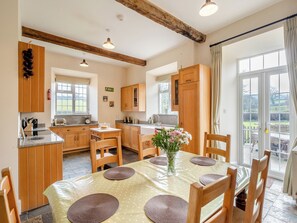 Una cocina con armarios de madera, una mesa de comedor con individuales y vistas al exterior a través de una puerta de cristal.