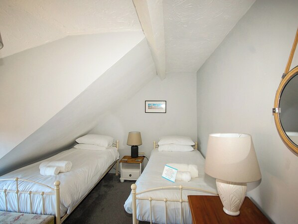 A small, triangular room with two single beds, a bedside table with a lamp, a small picture on the wall, and a round mirror.