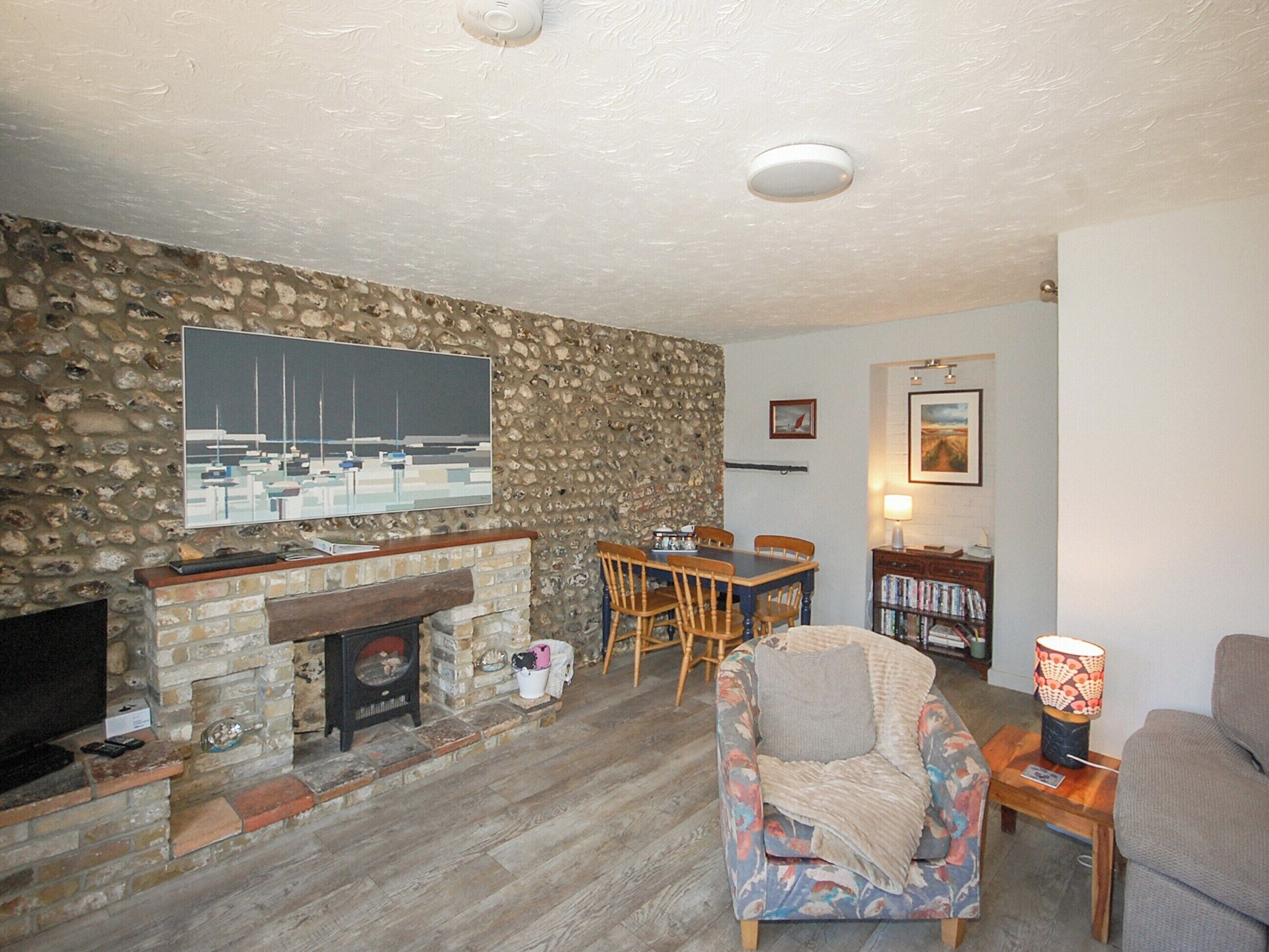 Una sala de estar con pared de piedra, chimenea, mesa de comedor con sillas, sofá y televisor montado en la pared.