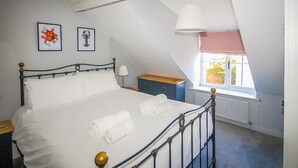 A bedroom with a bed, a nightstand, a lamp, a dresser, and a window with a view. - 2 bedroom accommodation in Wells-next-the-Sea (Wells-next-the-Sea)