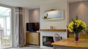 Una sala de estar moderna con una televisión de pantalla plana, una chimenea, una mesa de comedor con sillas y un ventanal con cortinas.