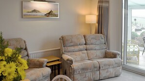 Una sala de estar con un sofá, una mesita y un sillón. Hay un cuadro en la pared y una lámpara junto al sofá.