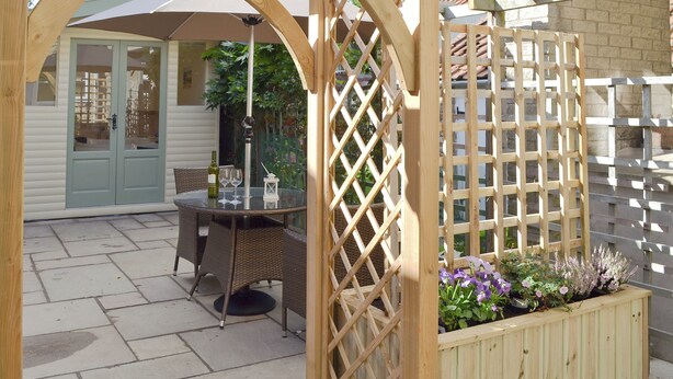 A wooden pergola structure, a patio table with wicker chairs, and a planter with flowers. - 1 bedroom accommodation in Sinnington near Pickering (Sinnington near Pickering)
