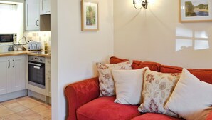 A cozy living room with a red sofa, a kitchen area with white cabinets, a toaster, and an oven. - 1 bedroom accommodation in Sinnington near Pickering (Sinnington near Pickering)