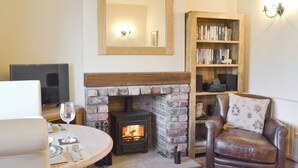 A living room with a fireplace, a leather armchair, a bookshelf, and a round table with a glass. - 1 bedroom accommodation in Sinnington near Pickering (Sinnington near Pickering)