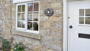 A stone cottage with a white door, a window with a white frame, and a sign reading 'Hill View Cottage.' There are two flower pots with plants in front of the cottage. - 1 bedroom accommodation in Sinnington near Pickering (Sinnington near Pickering)
