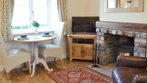 A cozy living room with a fireplace, a television, a dining table with chairs, and a window with curtains. - 1 bedroom accommodation in Sinnington near Pickering (Sinnington near Pickering)