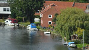 Un canal avec des bateaux, une maison rouge et un arbre.
