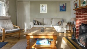 Un salon avec une table basse en bois, un canapé blanc, un fauteuil blanc, une cheminée et un tableau encadré au mur.