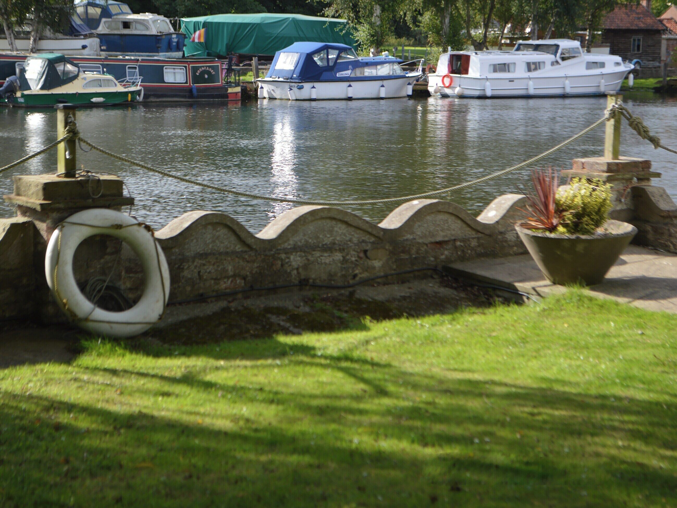 A canal with boats docked, a rope barrier, and a grassy area with a potted plant.