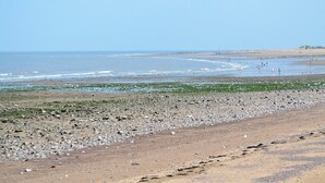 Ein felsiger Strand mit Wellen, einem klaren Himmel und Hügeln in der Ferne.