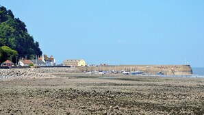Eine Küstenlandschaft mit steinigem Strand, einer hohen Urmauerung und mehreren vor Anker liegenden Booten.